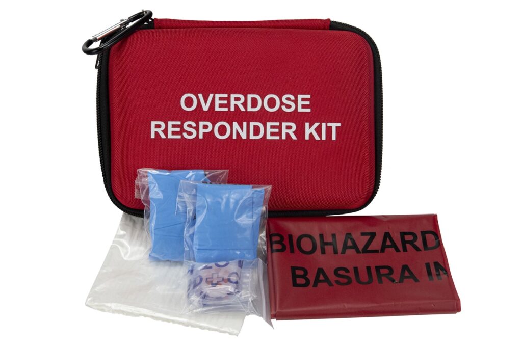 Overdose Responder Kit shown with included items: blue gloves, biohazard disposal bag, and other protective supplies arranged in front of the case.