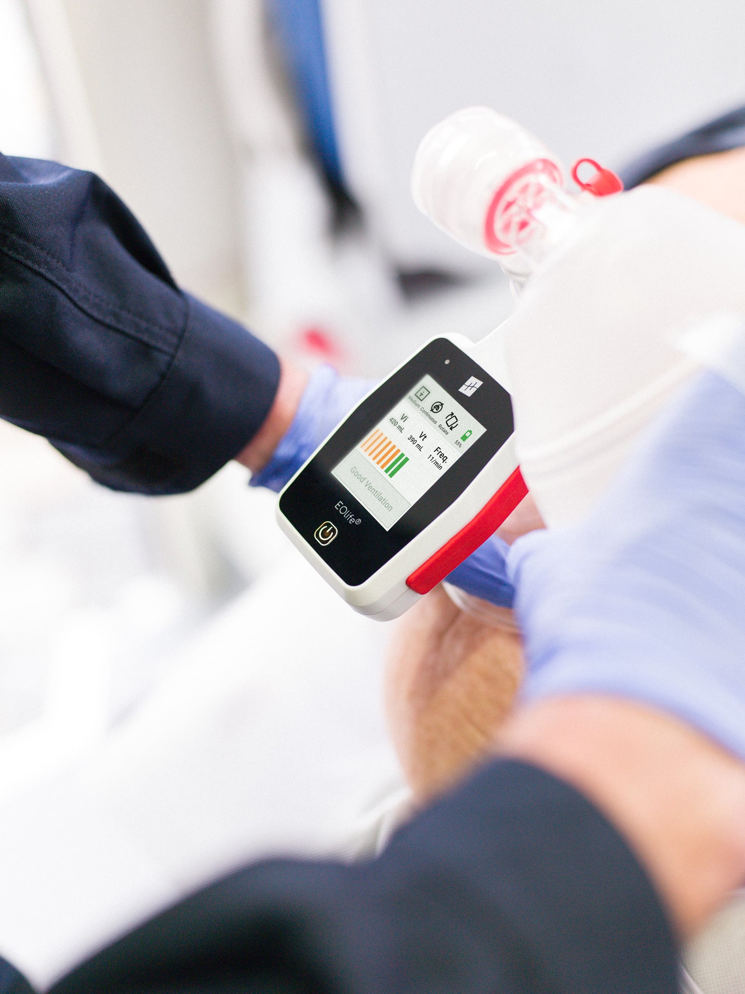 Close-up of an EOLife ventilation monitoring device displaying real-time feedback as a responder uses a bag-valve-mask on a patient.