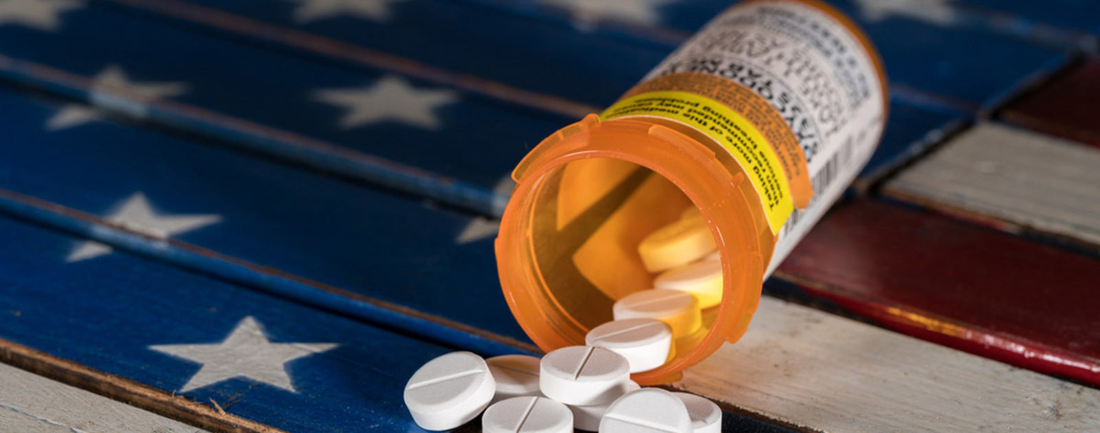 Prescription pill bottle spilling white tablets onto a wooden surface.